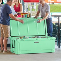 two men and a woman standing around a cooler