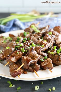 a plate full of beef skewers with green onions