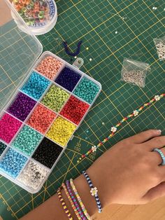 a person's hand on a table with beads and bead bracelets next to it