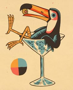 a bird sitting on top of a martini glass next to an orange and blue ball