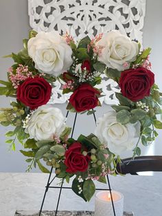 white and red roses arranged in a heart shaped arrangement on a table next to a lit candle