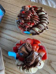 two desserts with strawberries and chocolate on them are sitting next to a cell phone