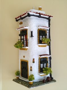 a white house with windows and plants on the top floor is hanging from a wall