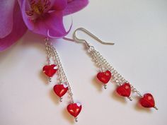 a pair of red heart - shaped dangling earrings on a white table next to a pink flower