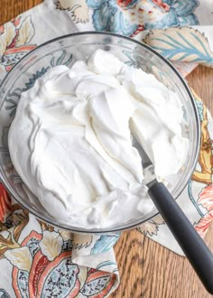 a glass bowl filled with whipped cream on top of a wooden table next to napkins