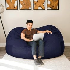 a young man sitting on a bean bag chair using a laptop computer while looking at the screen