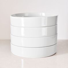 four white bowls stacked on top of each other in front of a white wall and floor