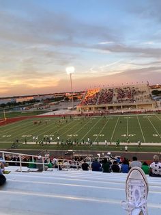 a person's feet are sitting on the bleachers watching a football game