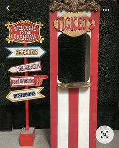 a red and white ticket booth sitting next to a green wall with signs on it