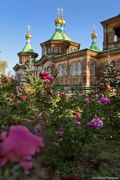 an old building with green roof and gold domes surrounded by pink flowers in the foreground