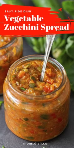 two jars filled with vegetable zucchini spread on top of a black surface next to green leaves