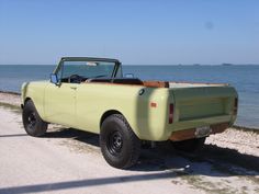 an old pick up truck parked on the side of the road near the water's edge