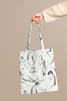 a woman's hand holding a tote bag with drawings on it