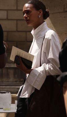 a woman in white shirt and black pants holding a book