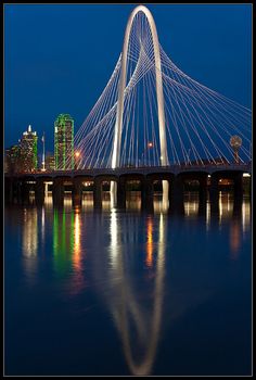 a bridge that is over some water with buildings in the backgrouds at night