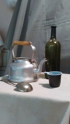 a tea kettle and cup sitting on top of a table next to a wine bottle