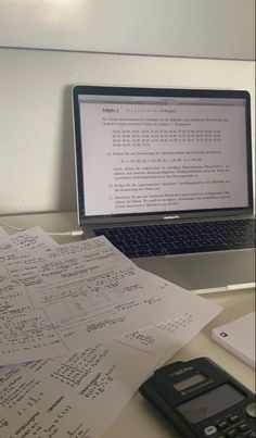 an open laptop computer sitting on top of a desk next to papers and a calculator