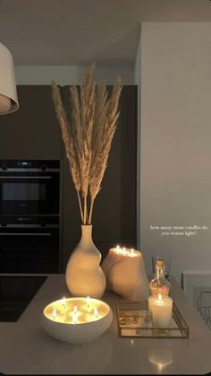 two white vases with lit candles in them on a counter top next to an oven