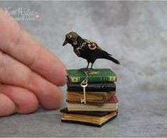 a tiny black bird sitting on top of a stack of books next to a person's hand