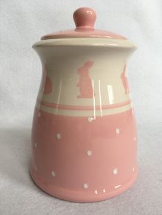 a pink and white ceramic pot with polka dot design on the bottom, sitting on a white surface