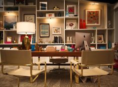 two chairs sitting in front of a desk with a lamp on it and bookshelves behind them