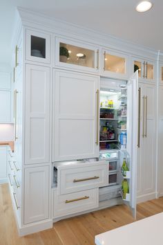 an open refrigerator in a white kitchen with wood flooring and cabinetry, along with wooden floors