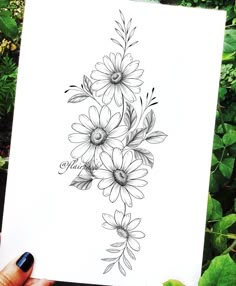 a person holding up a piece of paper with flowers drawn on it in front of some plants