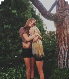 two girls hugging each other in front of trees