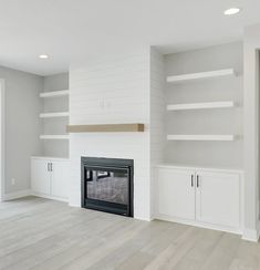 an empty living room with white painted walls and built in shelvings on either side of the fireplace