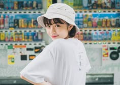 a woman standing in front of a vending machine wearing a white shirt and hat