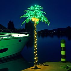 a lighted palm tree next to a boat docked in the water at night with lights on it