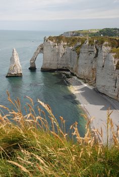 the beach is next to some very tall cliffs by the water with grass growing on it