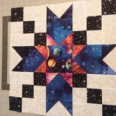 a quilted wall hanging on the side of a building with space and stars in it