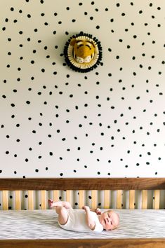 a baby laying on top of a bed next to a wall with black and white dots