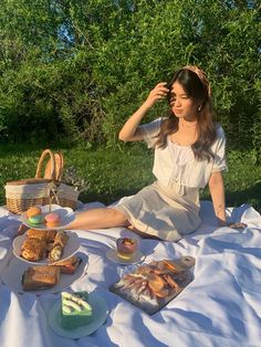 a woman sitting on the ground with food in front of her and picnic basket behind her