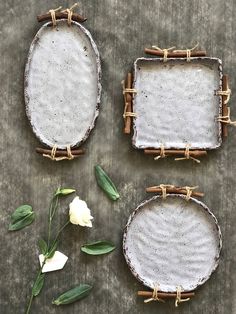 three white flowers sitting next to two small frames with sticks and leaves on the table