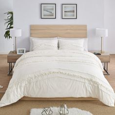 a bed with white comforter and pillows in a room next to two pictures on the wall