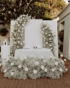 a table with white flowers and greenery on it in front of an outdoor setting