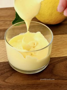 someone pouring cream into a glass bowl with a lemon in the background on a wooden table