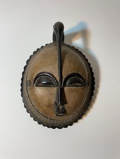 a decorative mask hanging on the wall in front of a white background with shadow coming from it