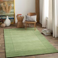 a green rug in a living room next to a chair, vases and books