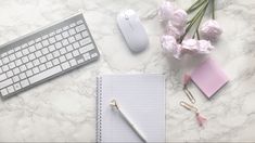 a keyboard, notepad and flowers on a marble surface