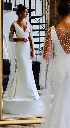 a woman standing in front of a mirror wearing a white dress with sheer sleeves and pearls on it