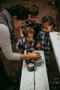 a woman and two boys are standing at a picnic table with food in tins