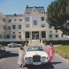 two women standing next to a white car in front of a large building