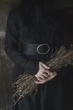 a woman in a black dress holding some dried grass and wearing a ring on her left hand