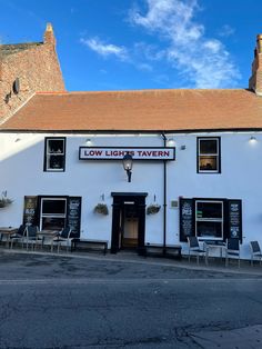 the exterior of low light tavern with tables and chairs on the outside, against a blue sky