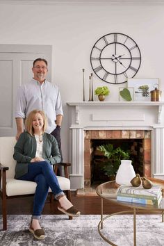 a man and woman are sitting in front of a fireplace with a clock on the wall behind them