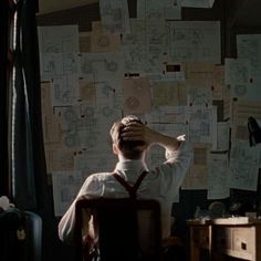 a man sitting at a desk in front of a wall covered with papers