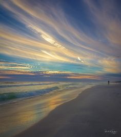 a person walking on the beach at sunset with colorful clouds in the sky above them